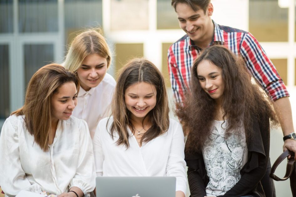 Grupa młodych, uśmiechniętych ludzi wpatruje się w ekran laptopa