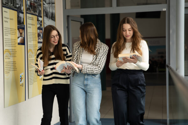 Trzy studentki idą korytarzem z książkami w rękach